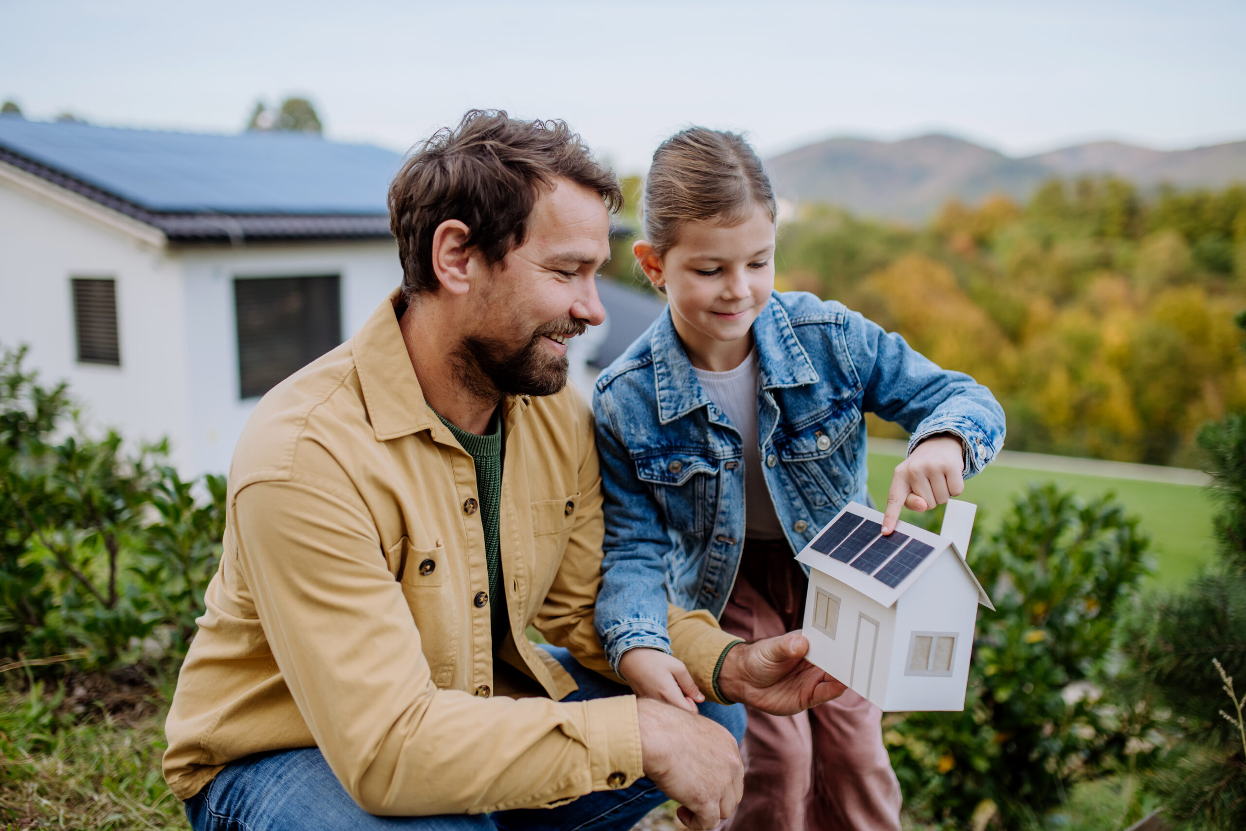 Little girl with her father holding paper model of house with the solar panels, explaining how it works.Alternative energy, saving resources and sustainable lifestyle concept.